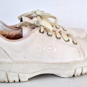 K&ouml;nnte beinhalten: Wei&szlig;e Canvas-Sneaker mit niedrigem Schaft, dicker wei&szlig;er Sohle und wei&szlig;en Schn&uuml;rsenkeln. Die Schuhe haben ein kleines wei&szlig;es Logo an der Seite.