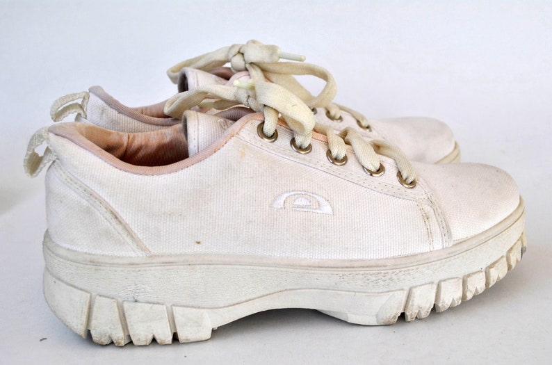 K&ouml;nnte beinhalten: Wei&szlig;e Canvas-Sneaker mit niedrigem Schaft, dicker wei&szlig;er Sohle und wei&szlig;en Schn&uuml;rsenkeln. Die Schuhe haben ein kleines wei&szlig;es Logo an der Seite.