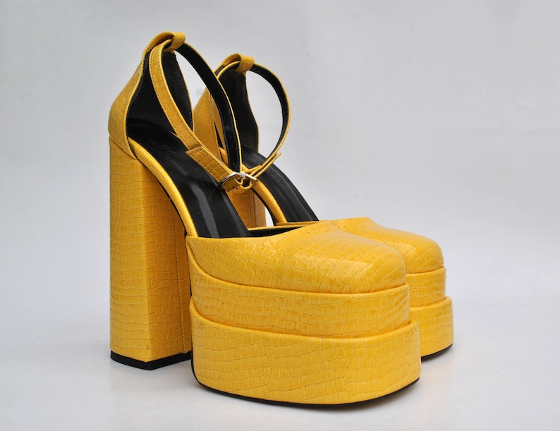 May include: A pair of yellow platform heels with ankle straps. The heels are made of a textured material that resembles crocodile skin.