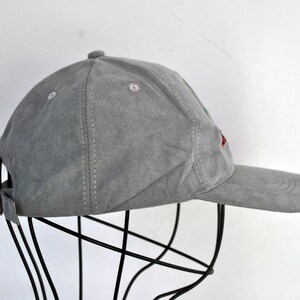 May include: A gray suede baseball cap with red and green embroidery. The cap is on a black stand.