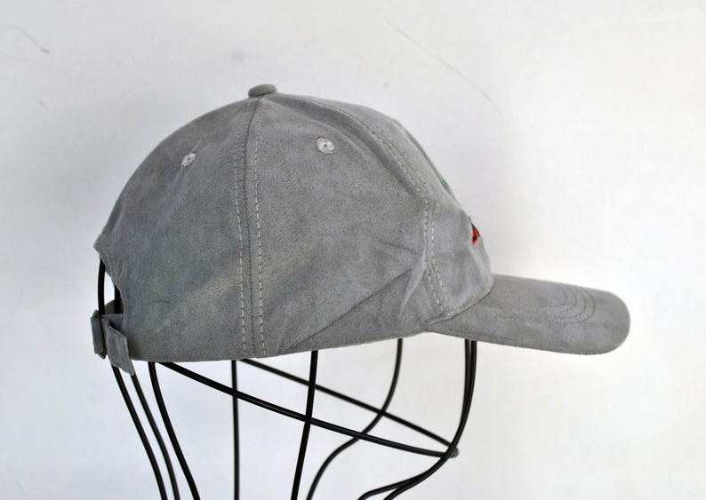 May include: A gray suede baseball cap with red and green embroidery. The cap is on a black stand.