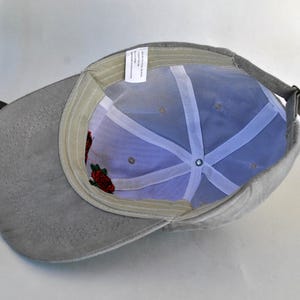 May include: A gray baseball cap with a mesh back and a floral embroidery design. The cap has a curved brim and a strap with a buckle.