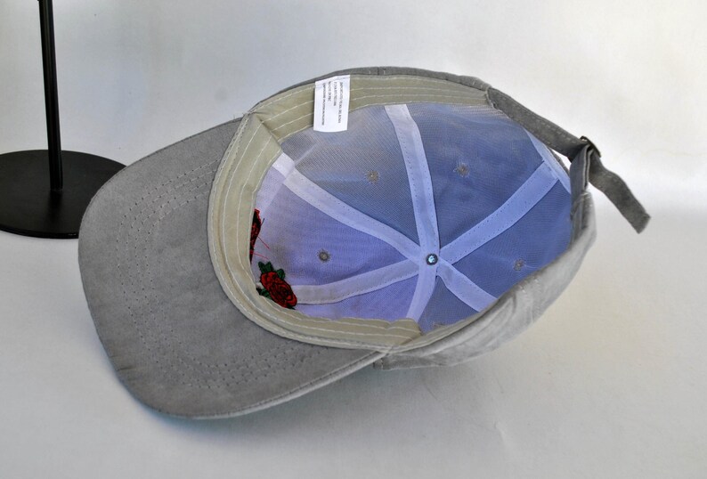 May include: A gray baseball cap with a mesh back and a floral embroidery design. The cap has a curved brim and a strap with a buckle.