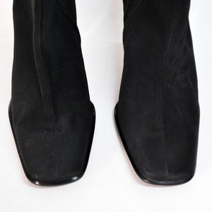 May include: A pair of black suede knee-high boots with a square toe.