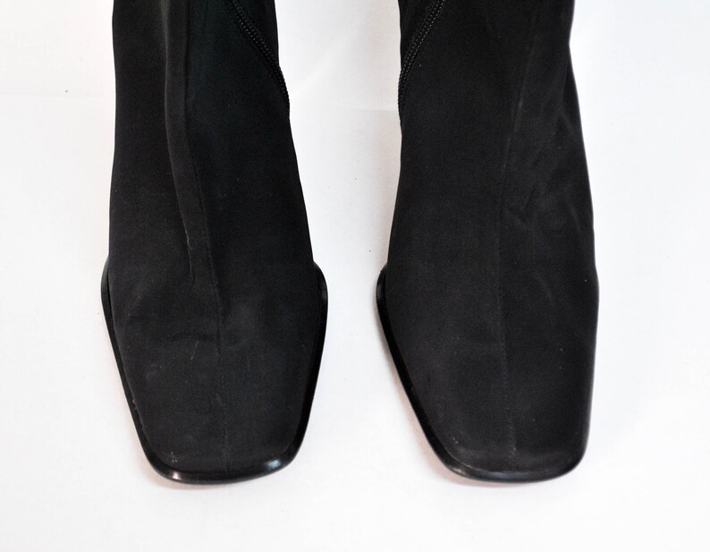 May include: A pair of black suede knee-high boots with a square toe.