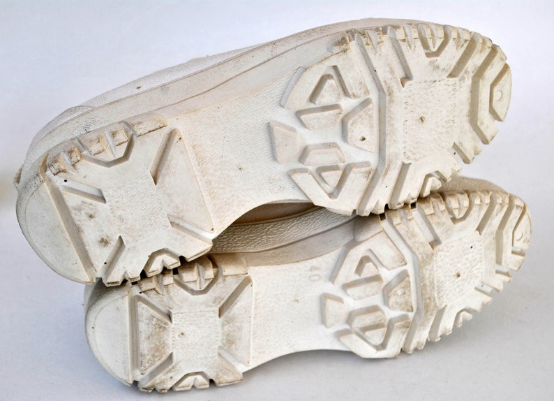 K&ouml;nnte beinhalten: Ein Paar wei&szlig;e Sneaker mit einer dicken, strukturierten Sohle. Die Sohlen sind schmutzig und weisen Gebrauchsspuren auf.