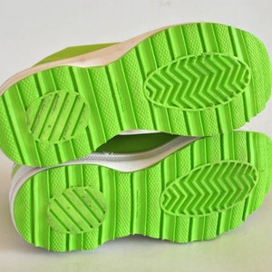 May include: Close-up of the bottom of a pair of bright green sneakers with white soles. The soles have a textured pattern and the words "Made in Italy" are printed on the bottom.