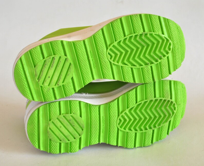 May include: Close-up of the bottom of a pair of bright green sneakers with white soles. The soles have a textured pattern and the words "Made in Italy" are printed on the bottom.