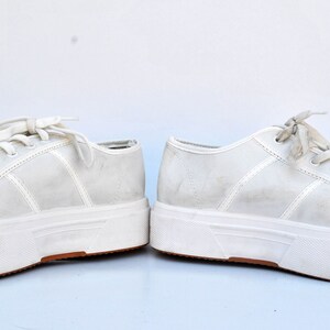 May include: A pair of white platform sneakers with white laces. The sneakers have a thick white sole and a slightly distressed look.