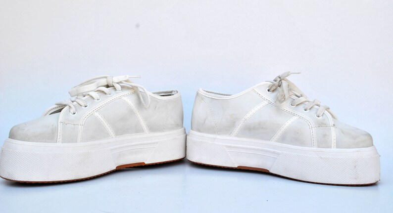May include: A pair of white platform sneakers with white laces. The sneakers have a thick white sole and a slightly distressed look.