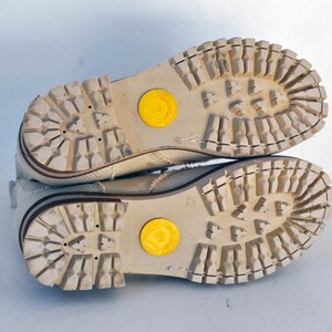 May include: A pair of white canvas shoes with brown rubber soles. The soles have a textured pattern and a yellow circle on each shoe.