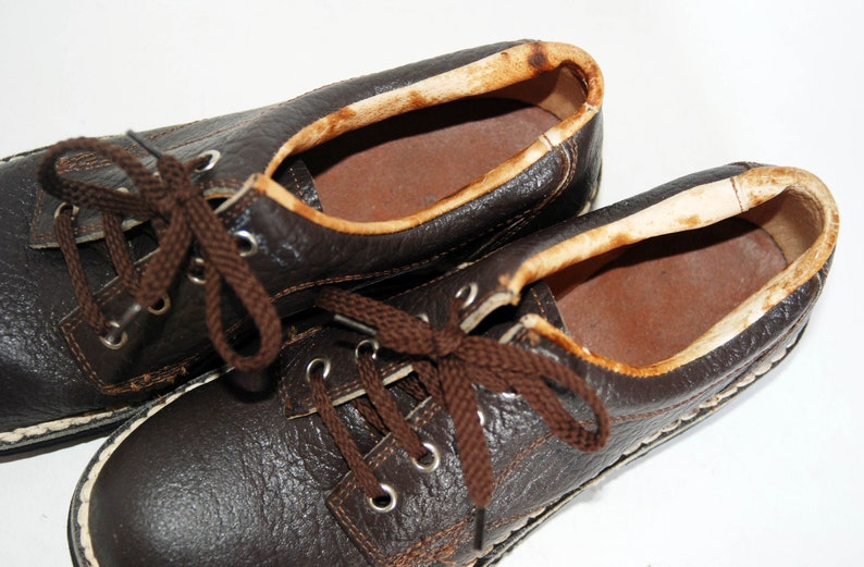 K&ouml;nnte beinhalten: Ein Paar braune Lederschn&uuml;rschuhe mit wei&szlig;en N&auml;hten an den R&auml;ndern. Die Schuhe haben braune Schn&uuml;rsenkel und sind abgenutzt.
