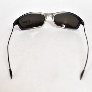 May include: A pair of black and silver sunglasses with a dark gray lens. The sunglasses have a thin, black frame and black arms.