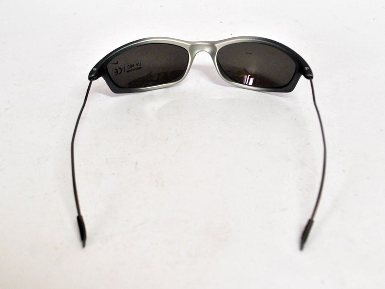 May include: A pair of black and silver sunglasses with a dark gray lens. The sunglasses have a thin, black frame and black arms.