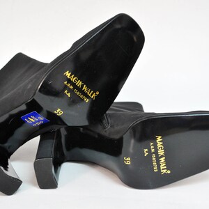 May include: A pair of black ankle boots with a block heel. The boots have a gold label on the back that reads "Magik Walk" with the text "A.G.M. 15858793 K.A. 39".
