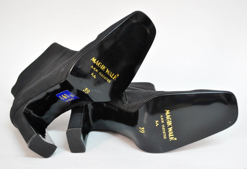 May include: A pair of black ankle boots with a block heel. The boots have a gold label on the back that reads "Magik Walk" with the text "A.G.M. 15858793 K.A. 39".