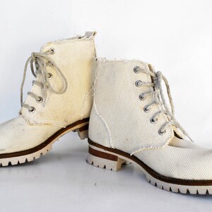 May include: A pair of white canvas lace-up boots with brown soles. The boots have a casual, rugged look.