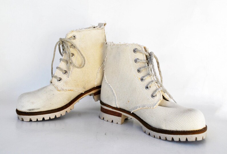 May include: A pair of white canvas lace-up boots with brown soles. The boots have a casual, rugged look.