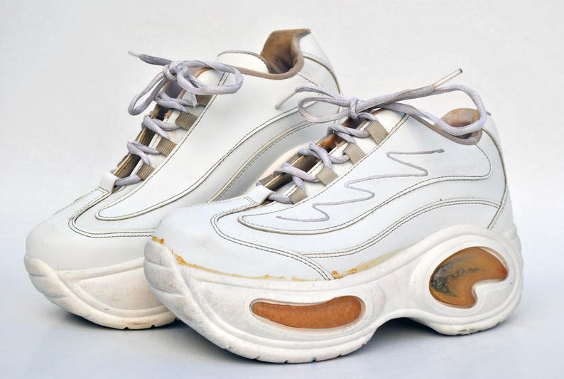 Puede incluir: Un par de zapatillas blancas de plataforma con suela gruesa y cierre de cordones. Las zapatillas tienen un aspecto ligeramente desgastado, con algunas rozaduras y marcas en el cuero.