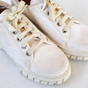 K&ouml;nnte beinhalten: Ein Paar wei&szlig;e Canvas-Sneaker mit wei&szlig;en Schn&uuml;rsenkeln und einer dicken wei&szlig;en Gummisohle.