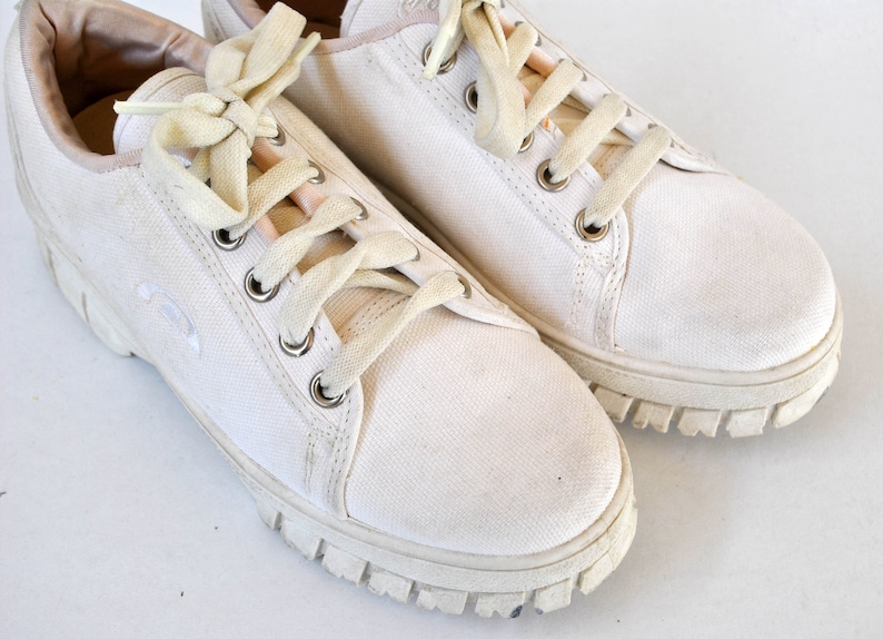 K&ouml;nnte beinhalten: Ein Paar wei&szlig;e Canvas-Sneaker mit wei&szlig;en Schn&uuml;rsenkeln und einer dicken wei&szlig;en Gummisohle.