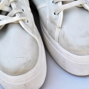 May include: A pair of white canvas sneakers with white laces. The sneakers have a worn look and are slightly dirty.