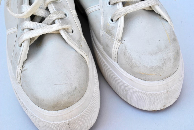 May include: A pair of white canvas sneakers with white laces. The sneakers have a worn look and are slightly dirty.
