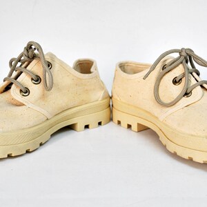 May include: A pair of off-white canvas shoes with thick, white rubber soles and brown laces.