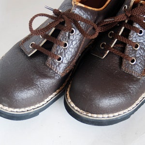 K&ouml;nnte beinhalten: Ein Paar braune Lederschn&uuml;rschuhe mit wei&szlig;en N&auml;hten an den R&auml;ndern. Die Schuhe haben ein strukturiertes Obermaterial aus Leder und eine dunkelbraune Sohle.