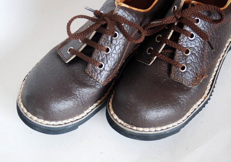 K&ouml;nnte beinhalten: Ein Paar braune Lederschn&uuml;rschuhe mit wei&szlig;en N&auml;hten an den R&auml;ndern. Die Schuhe haben ein strukturiertes Obermaterial aus Leder und eine dunkelbraune Sohle.