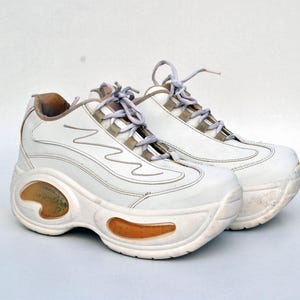 Puede incluir: Un par de zapatillas blancas de plataforma con suela gruesa y cierre de cordones blanco.