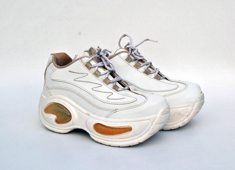 Puede incluir: Un par de zapatillas blancas de plataforma con suela gruesa y cierre de cordones blanco.