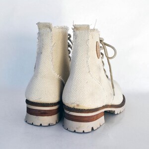 May include: A pair of white canvas high-top boots with brown leather accents and laces. The boots have a rugged look and are made of a durable material.