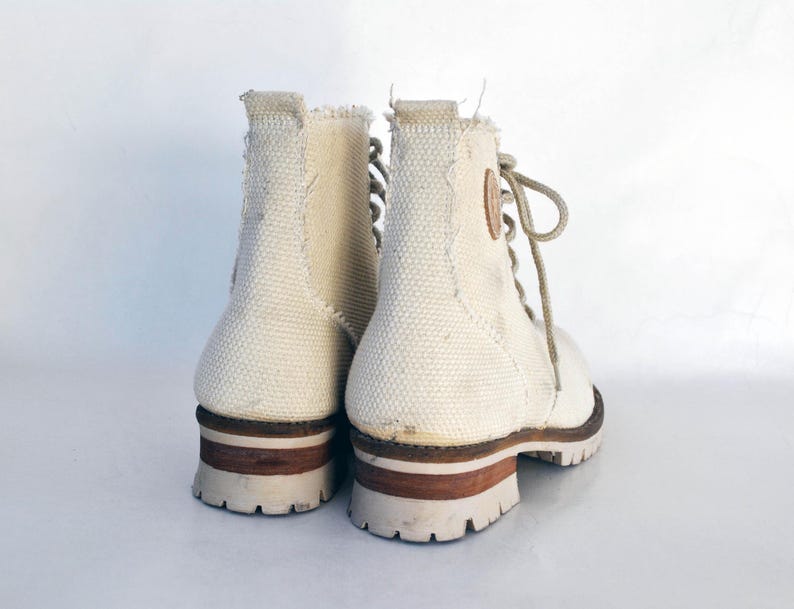 May include: A pair of white canvas high-top boots with brown leather accents and laces. The boots have a rugged look and are made of a durable material.