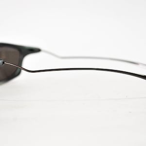 May include: A pair of black sunglasses with a thin metal frame and dark gray lenses. The sunglasses have a CE marking on the side.