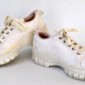 K&ouml;nnte beinhalten: Ein Paar wei&szlig;e Canvas-Plattform-Sneaker mit wei&szlig;en Schn&uuml;rsenkeln. Die Sneaker haben eine dicke Plattformsohle.