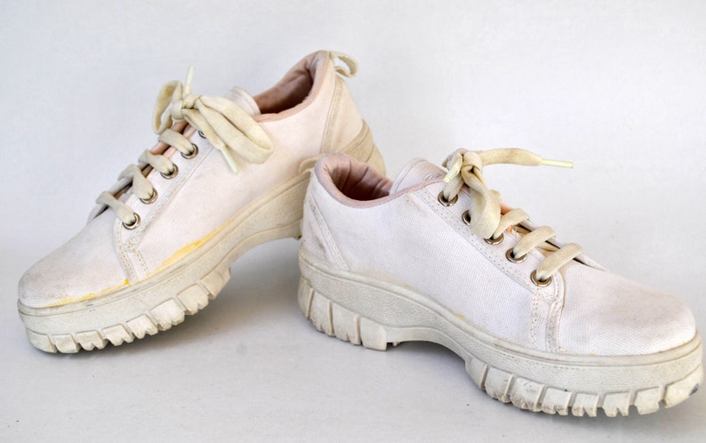 K&ouml;nnte beinhalten: Ein Paar wei&szlig;e Canvas-Plattform-Sneaker mit wei&szlig;en Schn&uuml;rsenkeln. Die Sneaker haben eine dicke Plattformsohle.