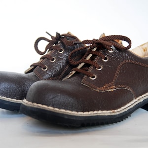 K&ouml;nnte beinhalten: Ein Paar braune Lederschn&uuml;rschuhe mit wei&szlig;en N&auml;hten um die Sohle. Die Schuhe haben ein robustes Aussehen und sind aus strukturiertem Leder gefertigt.