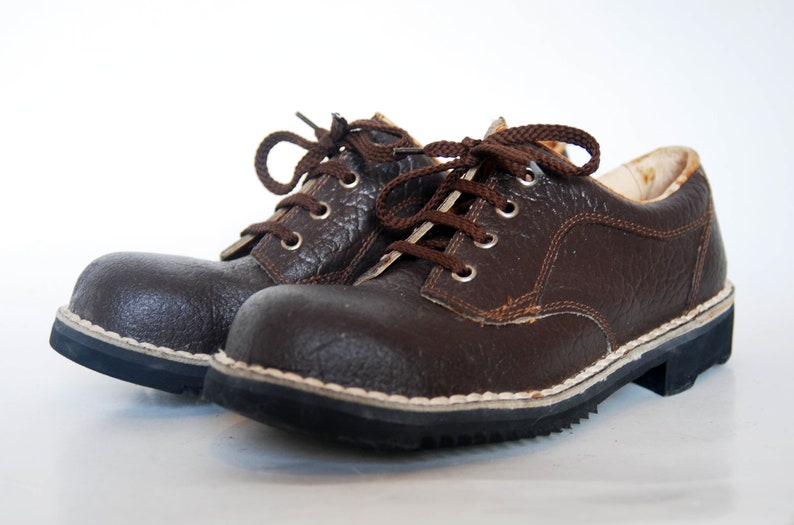 K&ouml;nnte beinhalten: Ein Paar braune Lederschn&uuml;rschuhe mit wei&szlig;en N&auml;hten um die Sohle. Die Schuhe haben ein robustes Aussehen und sind aus strukturiertem Leder gefertigt.