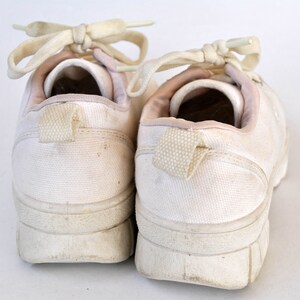 K&ouml;nnte beinhalten: Ein Paar wei&szlig;e Canvas-Sneaker mit wei&szlig;en Schn&uuml;rsenkeln. Die Sneaker haben ein schlichtes Design und sind abgenutzt.
