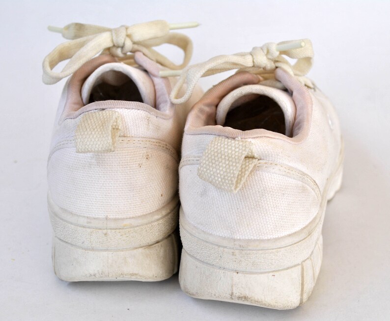 K&ouml;nnte beinhalten: Ein Paar wei&szlig;e Canvas-Sneaker mit wei&szlig;en Schn&uuml;rsenkeln. Die Sneaker haben ein schlichtes Design und sind abgenutzt.
