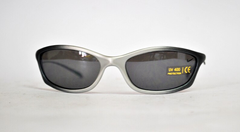 May include: Silver-framed sunglasses with dark gray lenses. The sunglasses have a UV 400 protection label and a CE mark.
