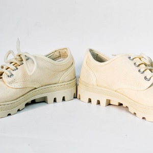 May include: A pair of off-white canvas shoes with thick white rubber soles and laces.