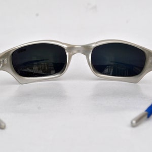 May include: Silver-toned sunglasses with blue rubber temple arms and dark gray lenses.
