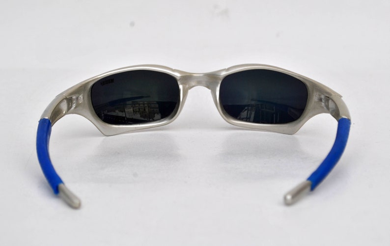 May include: Silver-toned sunglasses with blue rubber temple arms and dark gray lenses.