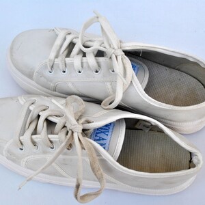 May include: A pair of white leather sneakers with white laces. The sneakers are worn and have some dirt on them.