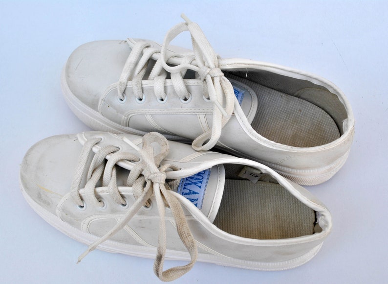 May include: A pair of white leather sneakers with white laces. The sneakers are worn and have some dirt on them.