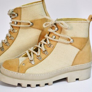 May include: A pair of beige canvas and suede hiking boots with white laces and a chunky white sole.