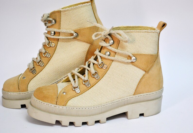 May include: A pair of beige canvas and suede hiking boots with white laces and a chunky white sole.