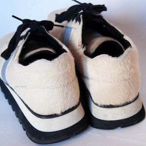 May include: A pair of white furry trainers with black laces and a black and white sole.